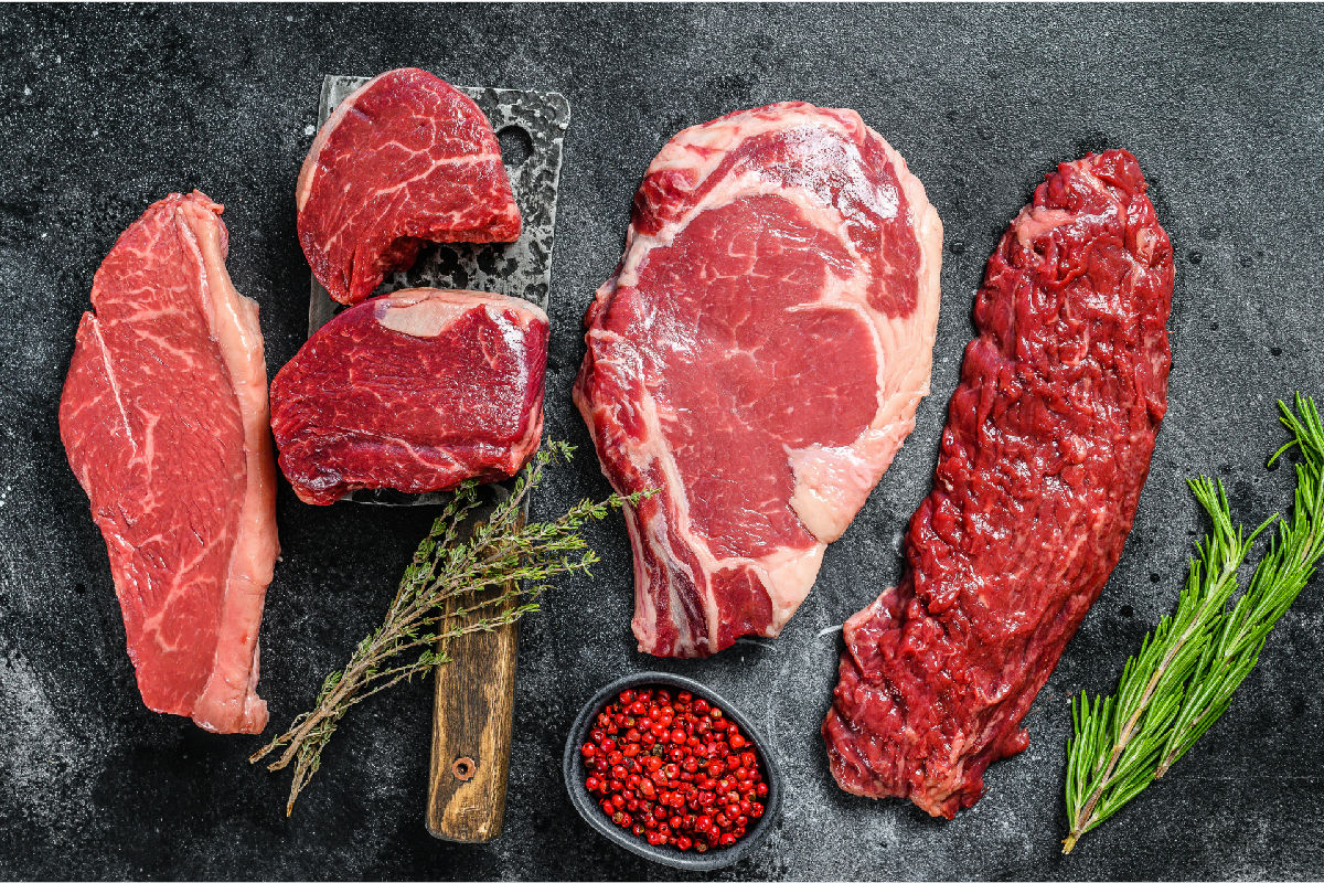 Verschiedene rohe Rindfleisch-Cuts mit Beil und Kräutern